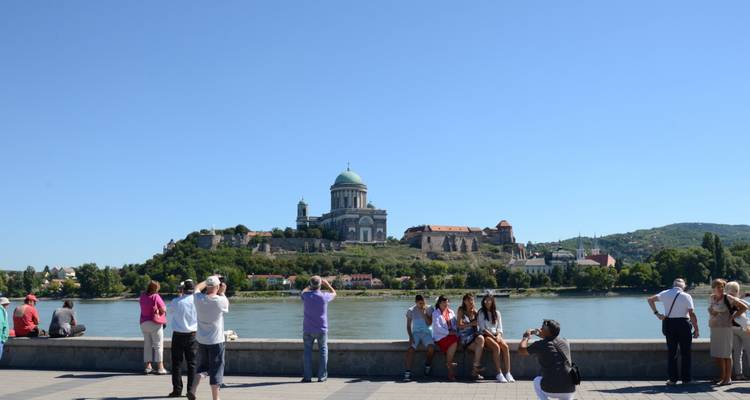 Des personnes assises au bord d'une rivière avec un bâtiment historique au loin.