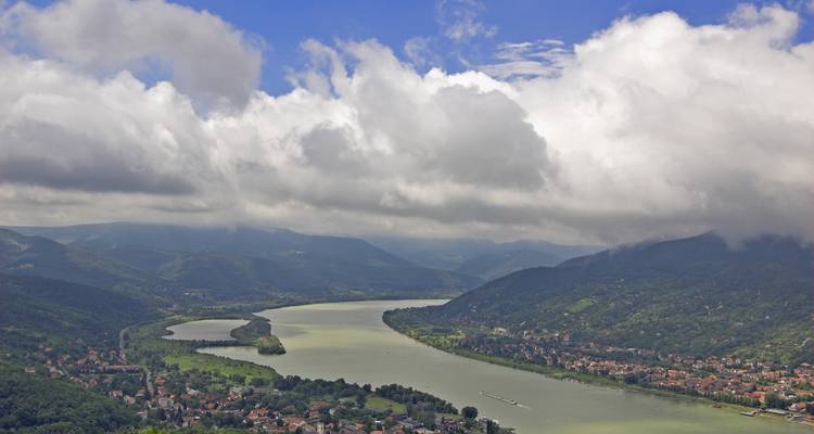 Vue aérienne d'une rivière serpentant à travers des collines verdoyantes luxuriantes sous un ciel partiellement nuageux.