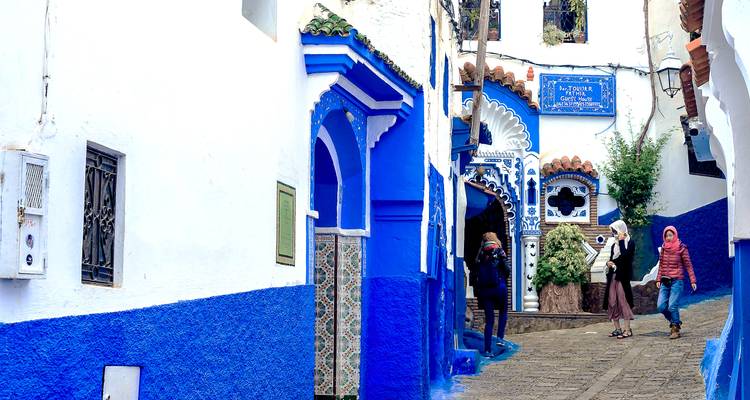 Eine malerische Straße in Chefchaouen mit blau gestrichenen Fassaden und gehenden Menschen.
