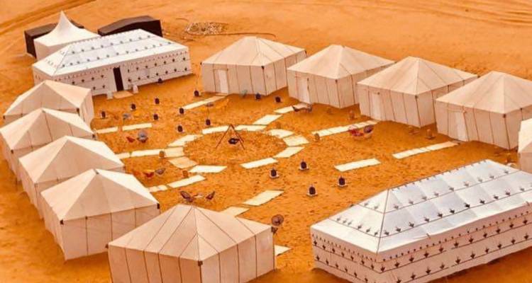 Vue aérienne d'un campement de luxe dans le désert avec des tentes blanches.