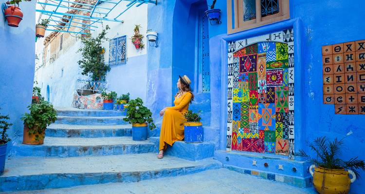 Mujer en un vestido amarillo sentada en una calle azul vibrante con decoraciones coloridas.