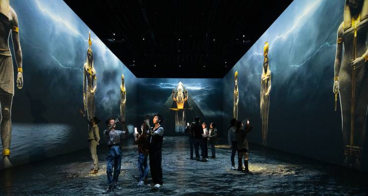 Des personnes observant une exposition immersive avec des projections d'imagerie de l'Égypte ancienne.