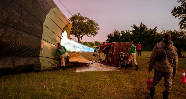 L'équipage gonfle un ballon à air chaud à l'aide de flammes dans la lumière précédant l'aube, tandis que d'autres observent.