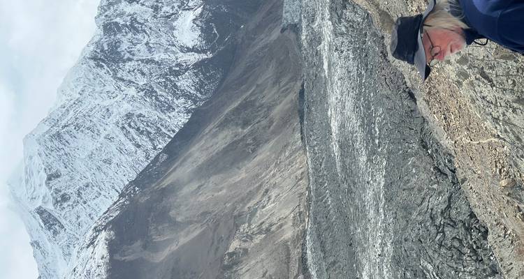Viajero mayor con sombrero contempla una áspera morrena glacial con altos picos nevados más allá