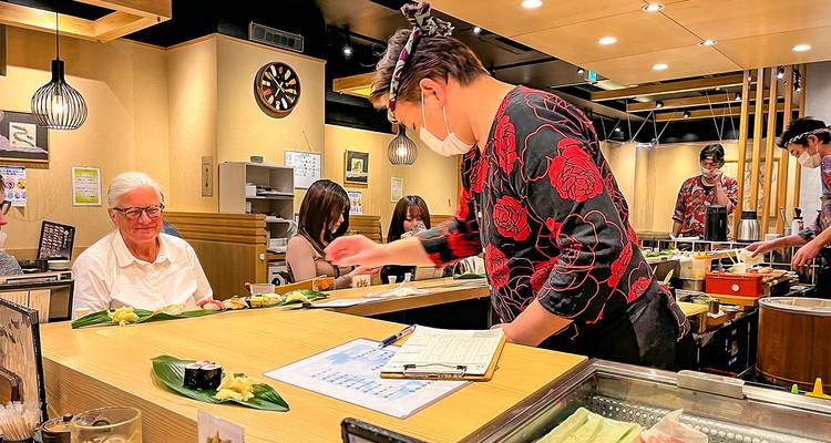 Chef de sushi préparant de la nourriture sous le regard des clients dans un cadre de restaurant chaleureux.