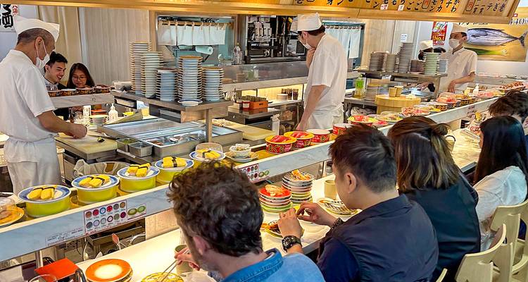 Des gens dégustant des sushis dans un restaurant de sushis à tapis roulant.