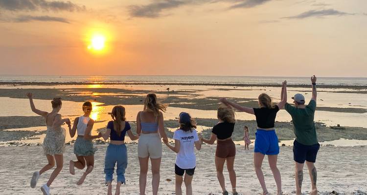 Groupe regardant le coucher de soleil sur une plage, sautant joyeusement.