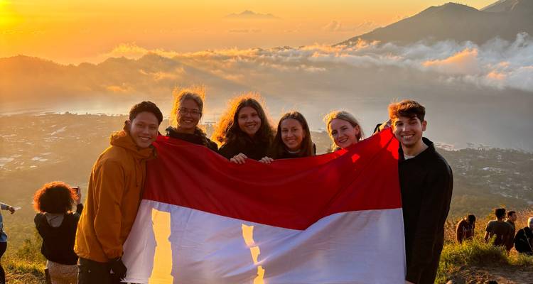 Groupe tenant un drapeau indonésien sur une montagne au lever du soleil.