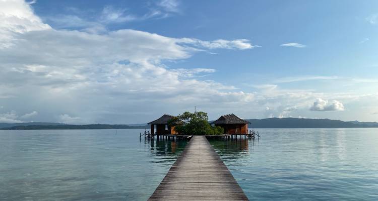 Jetée en bois menant à de petites cabanes au-dessus d'une eau tranquille.