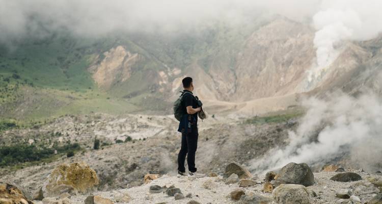 Excursionista admirando un paisaje montañoso escarpado con vapor elevándose.