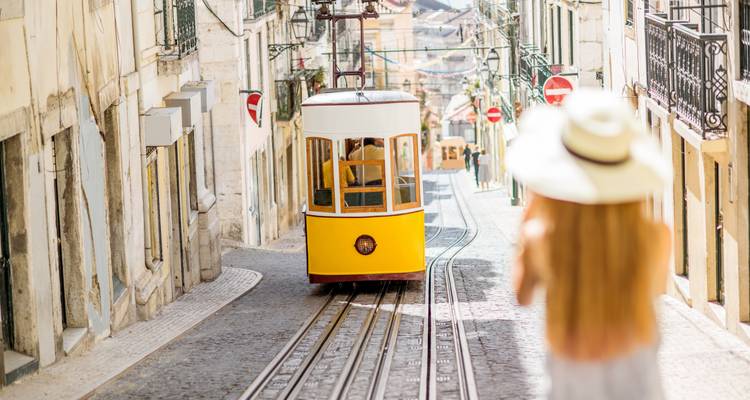 Een gele tram op een heuvelachtige straat met een persoon op de voorgrond.