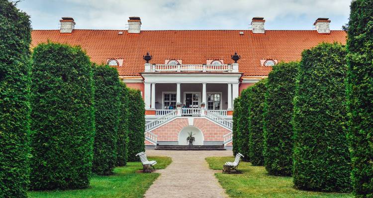 Un grand manoir avec des haies menant à l'entrée.