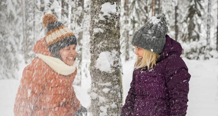 Zwei Personen in Winterkleidung in der Nähe eines schneebedeckten Baumes.
