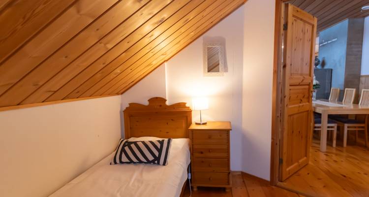 Einzelbett in einem hölzernen Dachzimmer mit Blick in einen anderen Raum.