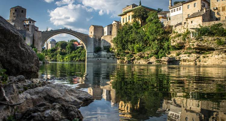 Mostars ikonische Brücke über einen Fluss mit üppigem Grün.