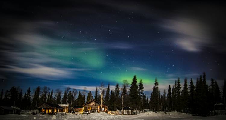 Aurores boréales au-dessus d'une cabane dans une forêt enneigée.
