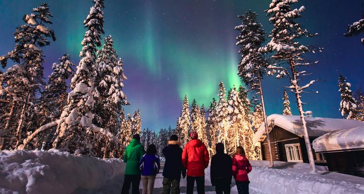 Groep mensen die het noorderlicht bekijkt boven een besneeuwde landschap.