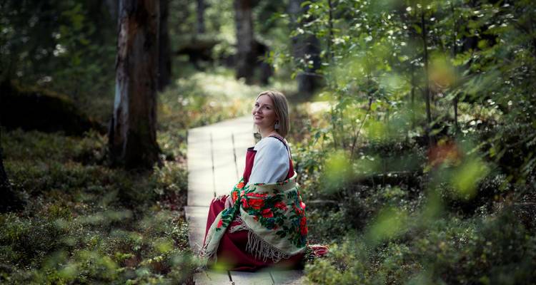 Femme en tenue traditionnelle assise dans une zone forestière.