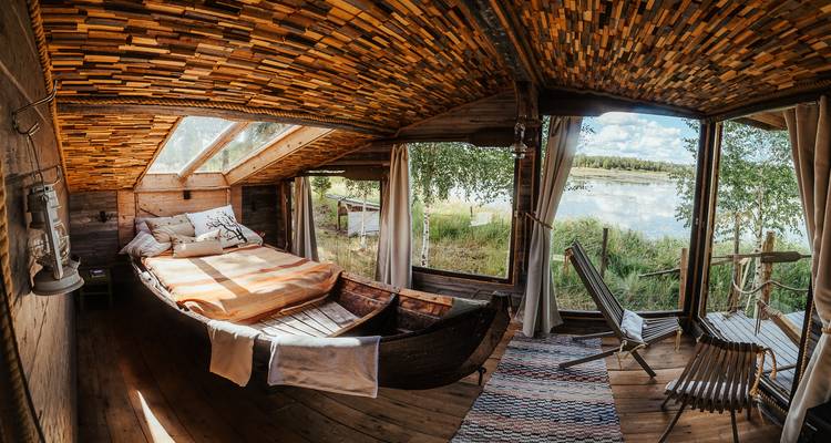 Intérieur rustique d'un chalet avec un lit et de grandes fenêtres donnant sur un lac.
