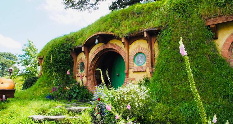 Trou de hobbit dans une verdure luxuriante avec des fleurs.