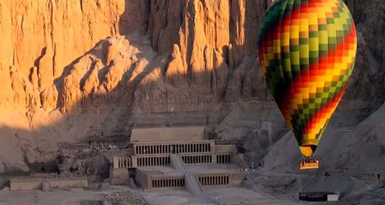 Heißluftballon über Wüstenlandschaft mit einem antiken Tempel.