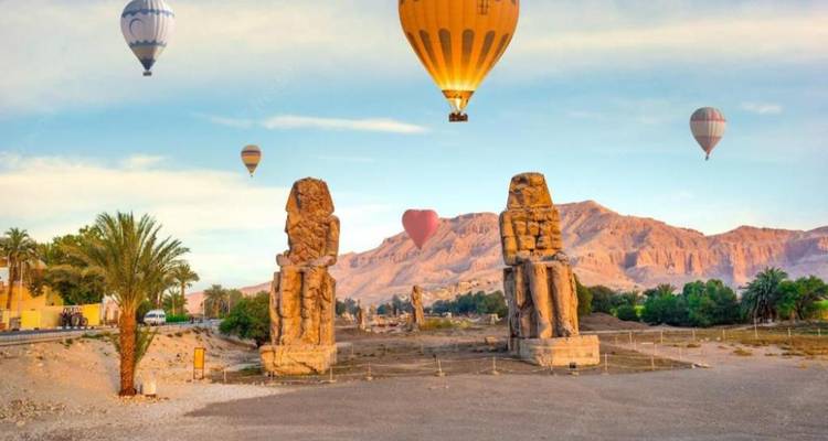 Mehrere Heißluftballons fliegen über Statuen mit entfernten Bergen.