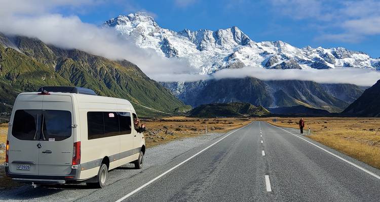 Busje geparkeerd op een lange weg met besneeuwde bergen.
