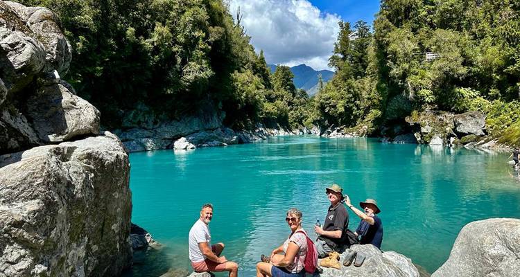 Grupo de personas sentadas junto a un río turquesa en un bosque.