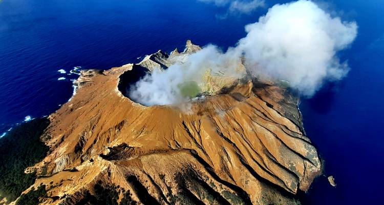Luchtfoto van een vulkanisch eiland met rook die uit de krater oprijst.