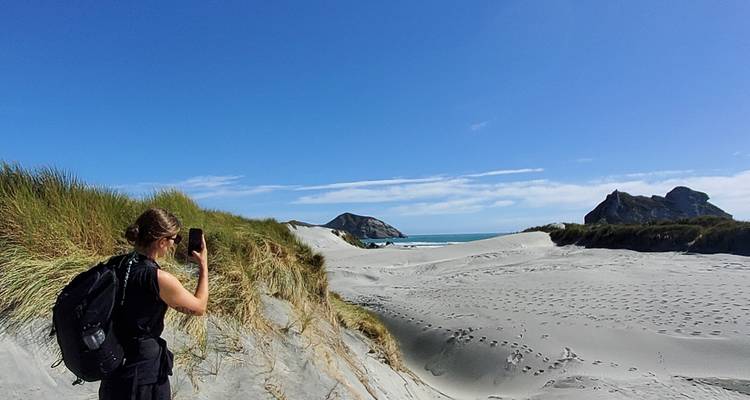 Wandelaar die een foto maakt op een zandig strand met duinen.