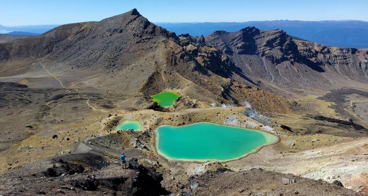 Turquoise alpine lakes with hikers on a rocky trail in a mountainous volcanic area.