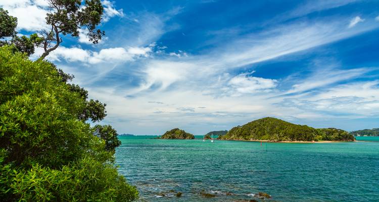 Scenic coastal view with green islands and turquoise water beneath wispy clouds.