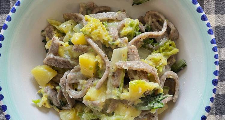 Gros plan d'un plat de pâtes traditionnel avec des légumes et de la sauce dans une assiette à bord bleu.