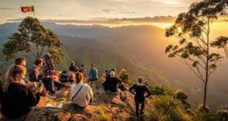 Groupe de personnes assises au bord d'une montagne profitant du lever du soleil.