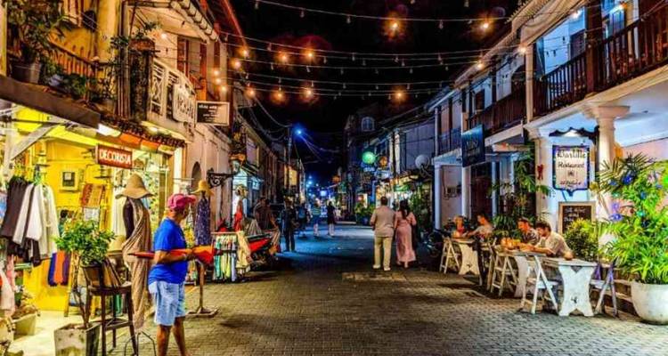 Marché de rue animé la nuit avec des lumières et des places assises extérieures.