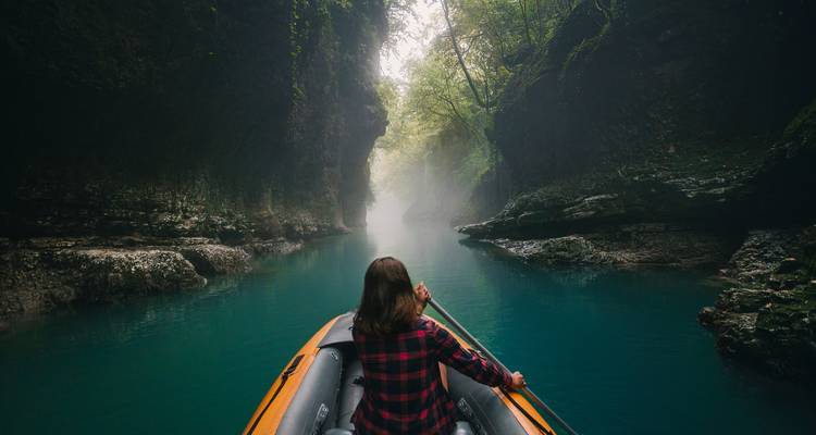 Une personne faisant du canoë à travers un canyon brumeux avec une végétation luxuriante.
