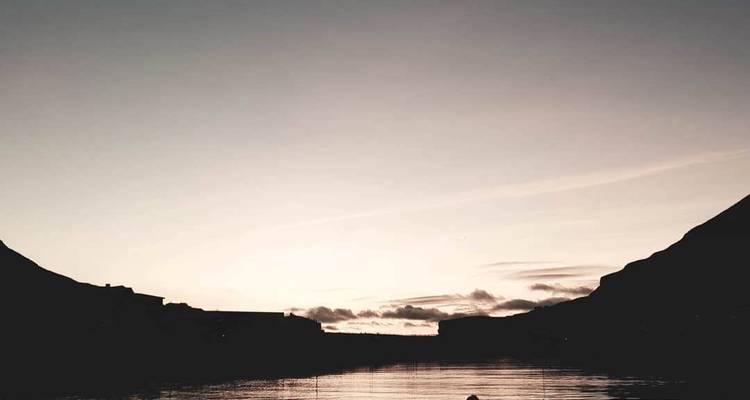 Vue crépusculaire avec des montagnes en silhouette et une étendue d'eau calme.