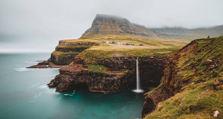 Cascade tombant dans l'océan entourée de falaises vertes.