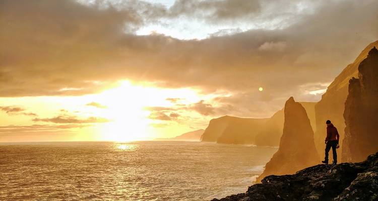 Une personne debout sur une falaise admirant un coucher de soleil sur l'océan.