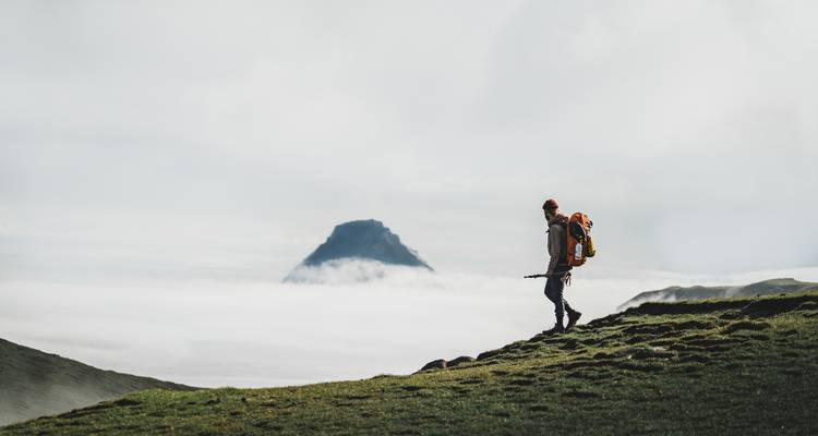 Un randonneur solitaire marchant le long d'un terrain herbeux avec une montagne en arrière-plan.
