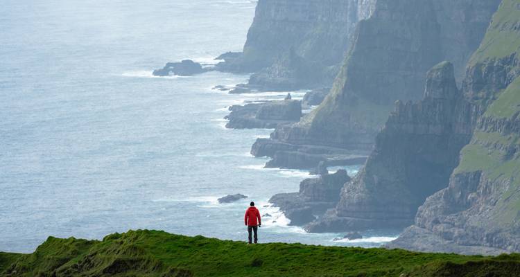 Une personne debout sur des falaises herbeuses surplombant l'océan et des falaises lointaines.