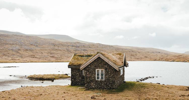 Maison en pierre avec un toit de chaume au bord d'un lac calme.