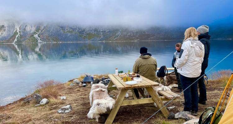 Groupe de personnes pique-niquant au bord d'un lac entouré de montagnes.