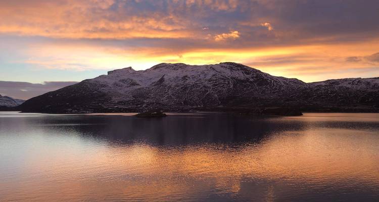 Un coucher de soleil se reflétant sur une étendue d'eau calme avec une montagne enneigée.