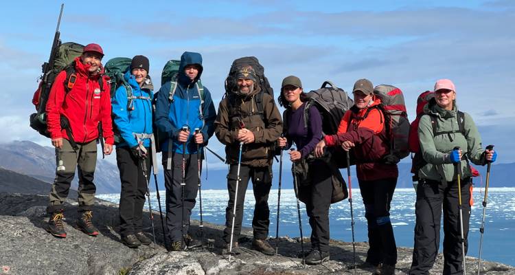 Un groupe de personnes avec de l'équipement de randonnée posant sur un terrain rocheux avec de la neige en arrière-plan.