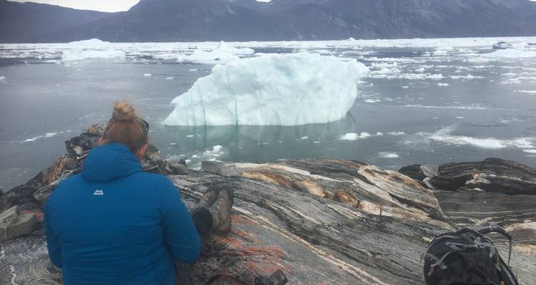 Une personne assise sur des rochers près de glace flottante dans un environnement froid.
