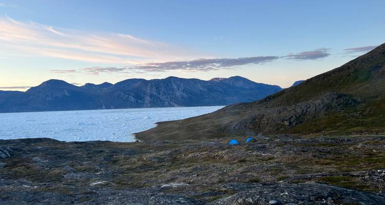 Tentes installées près d'un paysage gelé avec vue sur les montagnes au coucher du soleil.
