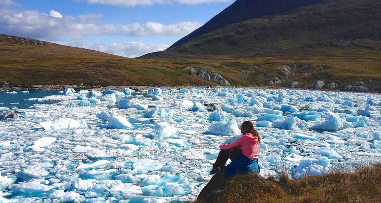 A person seated on a rock surrounded by a sea of icebergs.