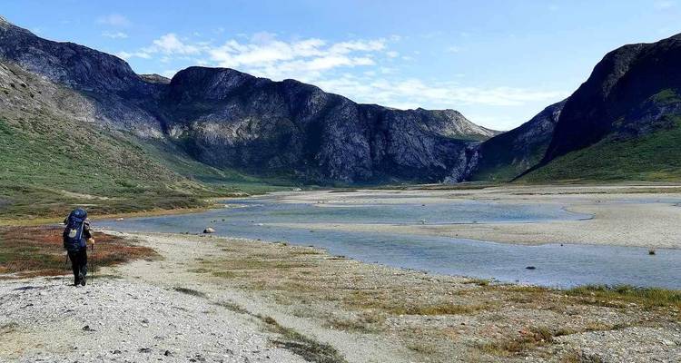 Solo hiker walking along a valley with a small stream.