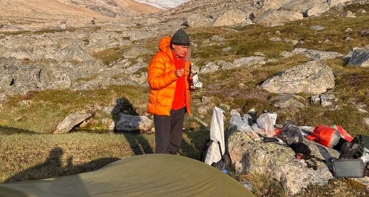 Person preparing a meal at a campsite on rocky terrain.